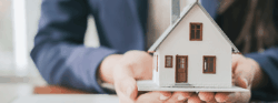 A person holding a small white model home in both of their hands.