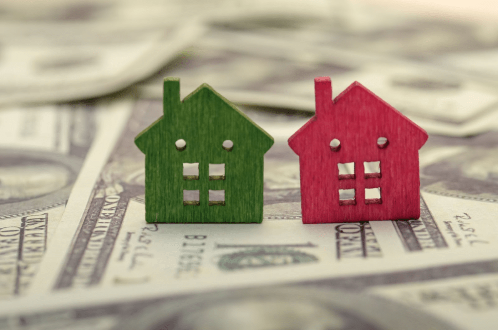 Red and green model homes next to each other on a stack of money