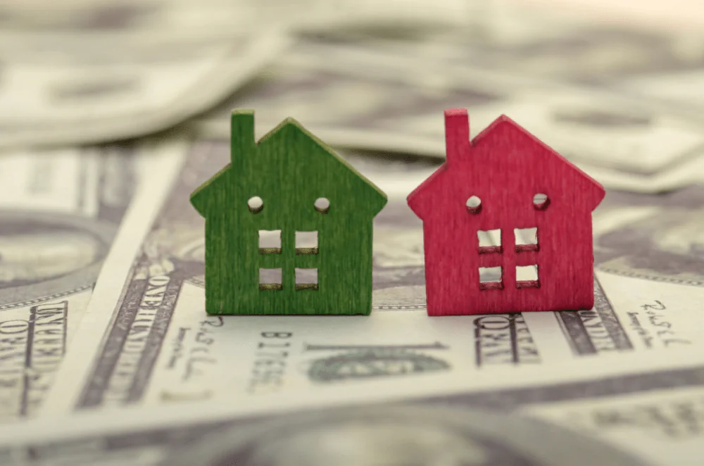 Red and green model homes next to each other on a stack of money