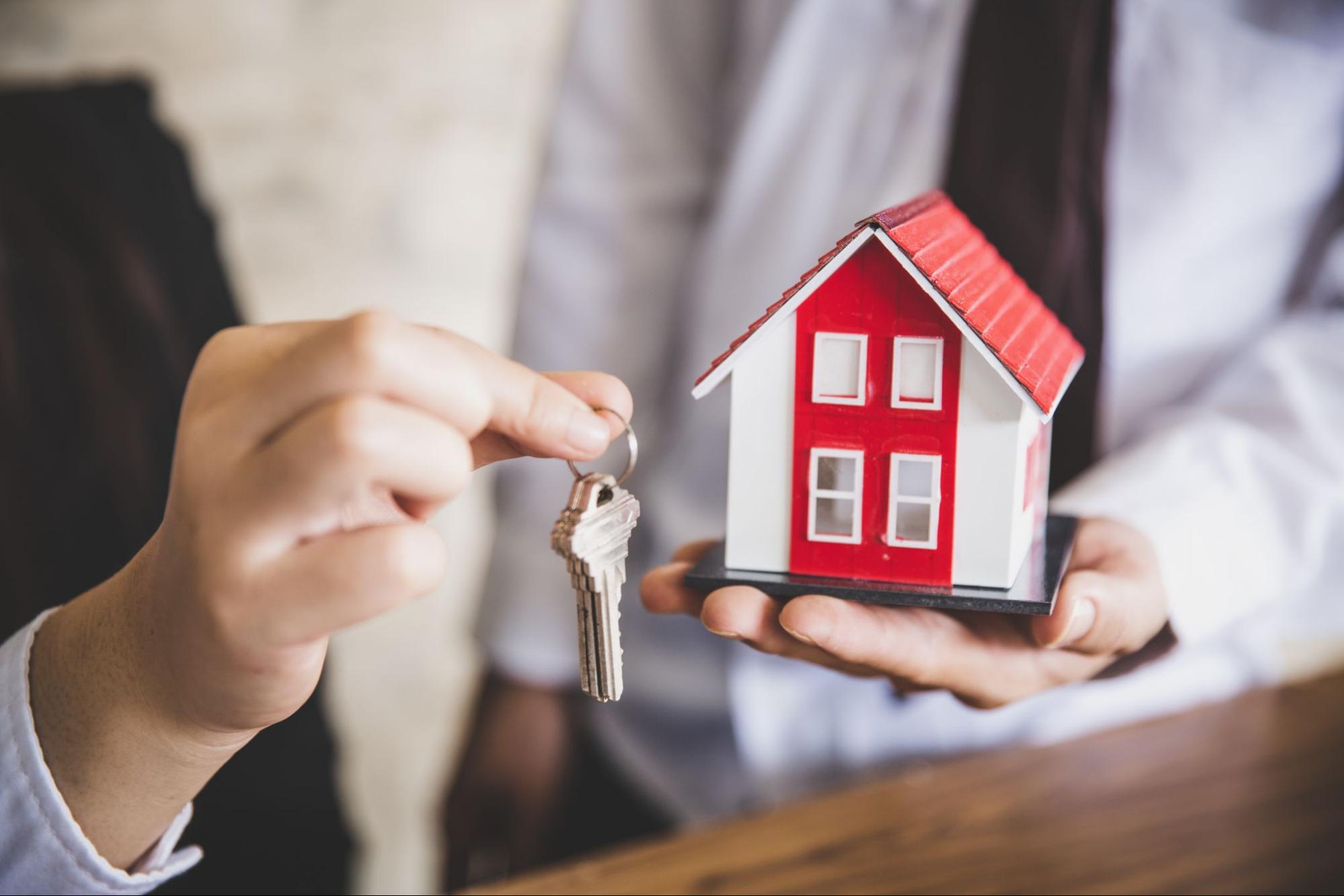 One person holding a red and white model home while another holds up a set of keys. 