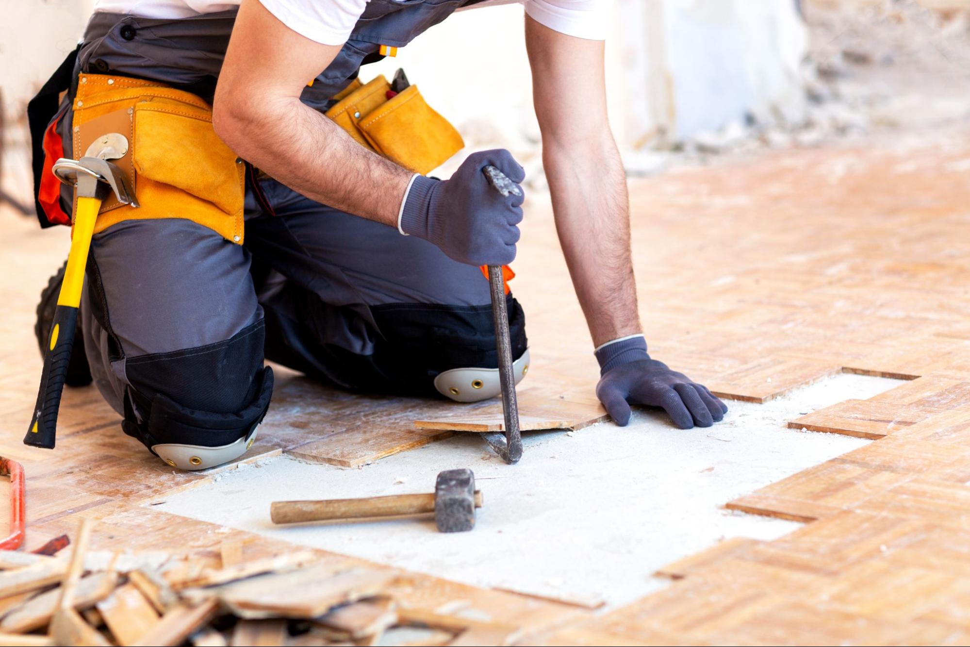 A contractor uses a tool to remove floorboards in a home.