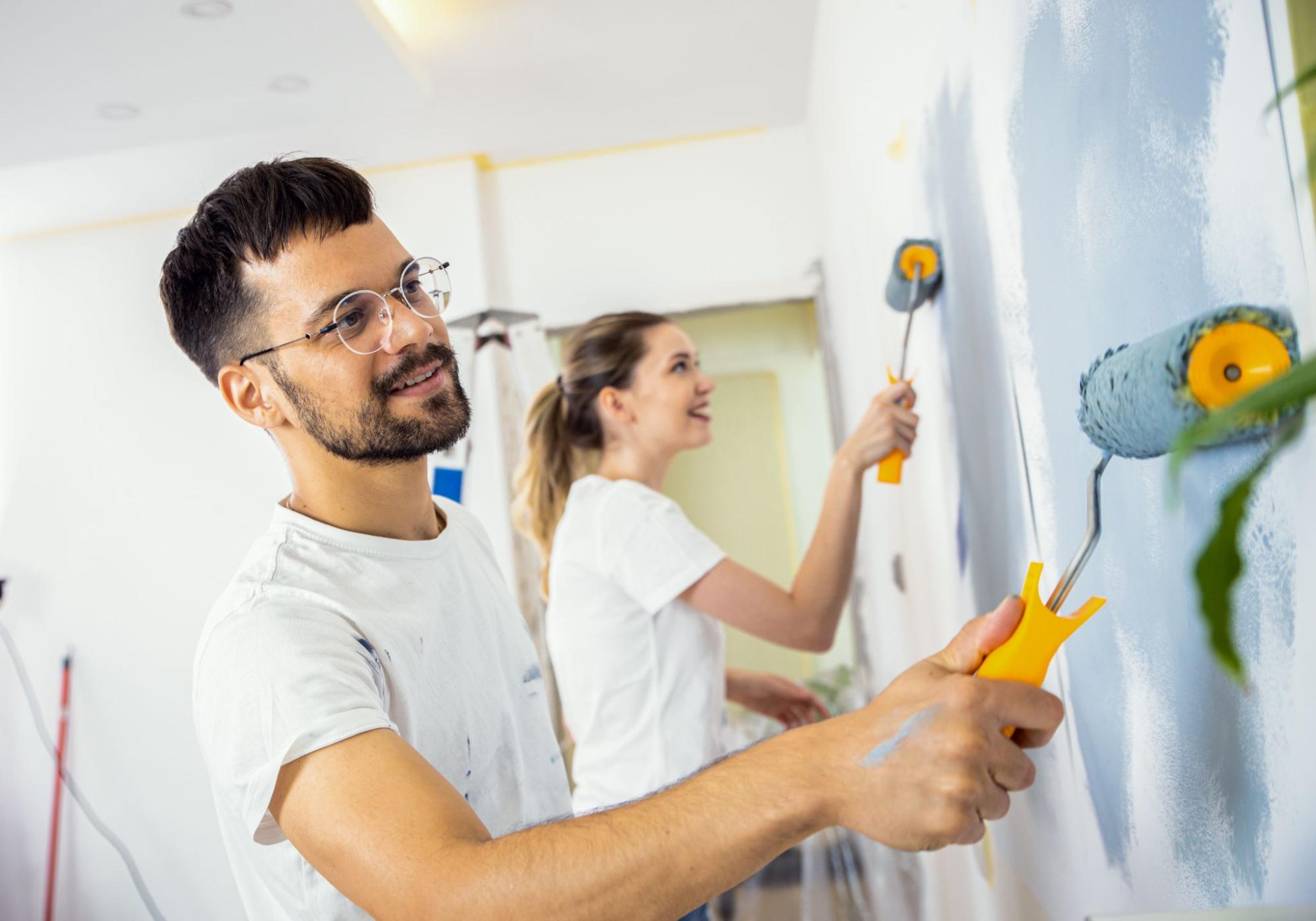 A young man and woman paint their walls blue.