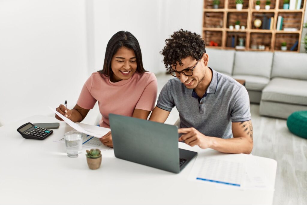 A young smiling couple reviews documents and works on a budget in their living room.