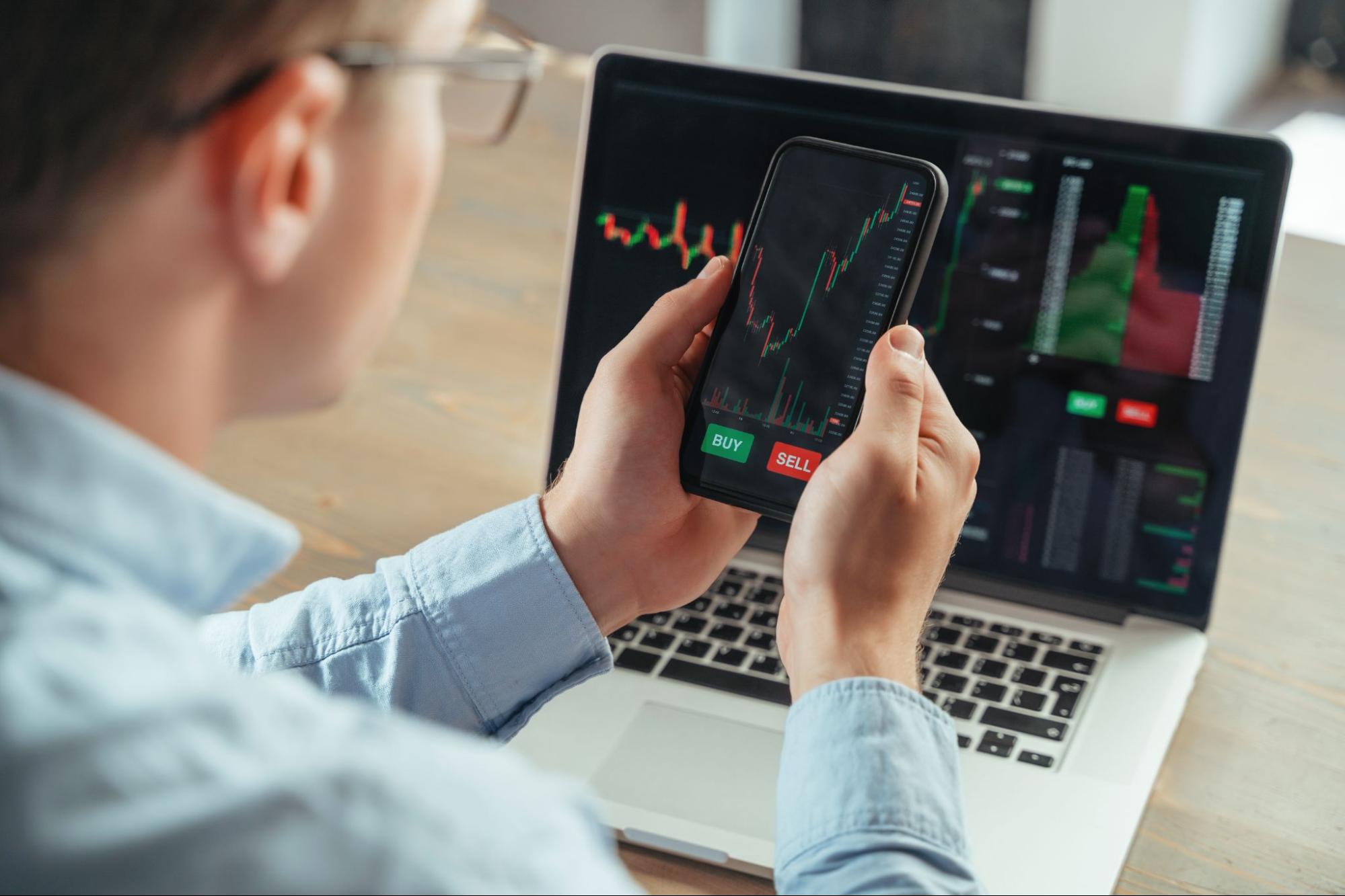 A man monitoring his crypto account on his phone and laptop.