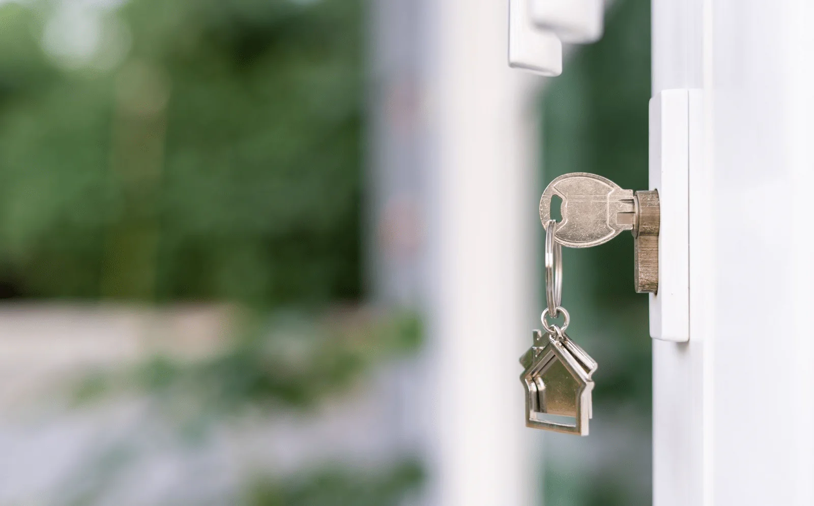 A key in a door with a metal house-shaped keychain attached. 