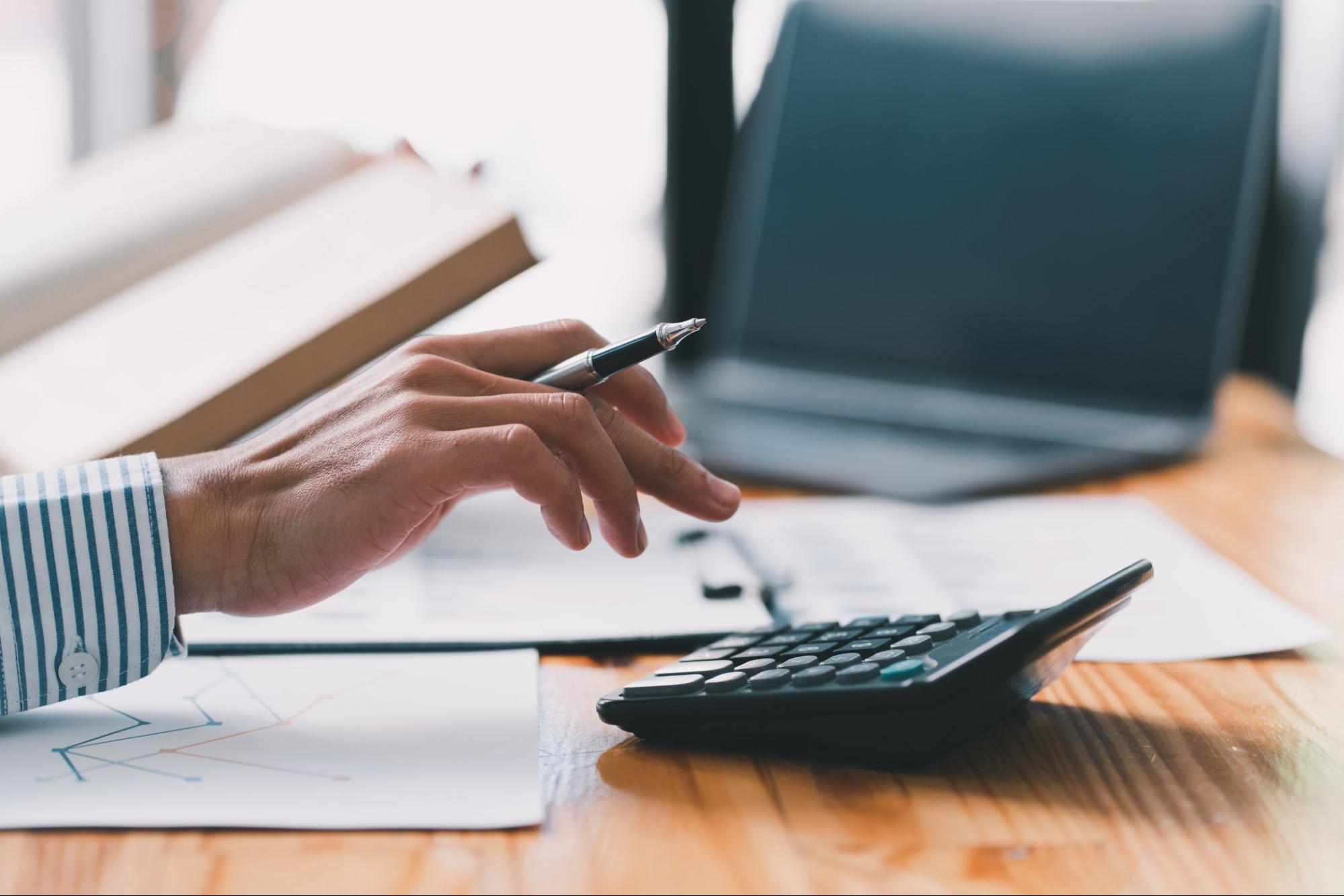 A person with a pen in hand using a calculator on their desk.