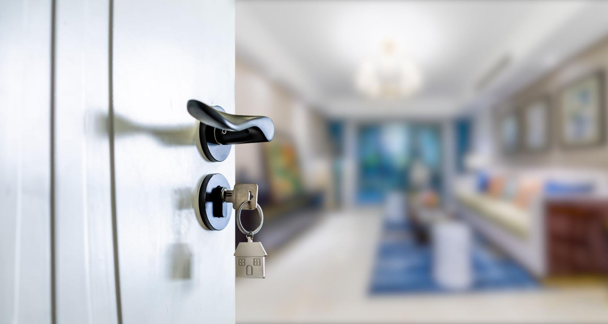 A house key in the lock of an open door leading to a living room.