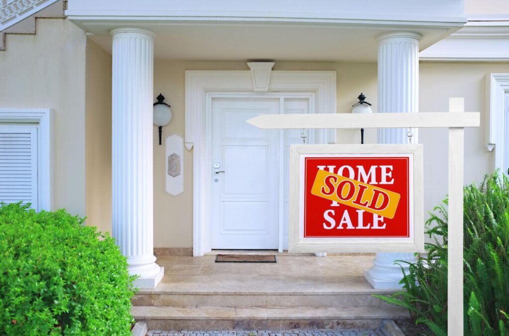 A white and tan colored home with green shrubs and a sold sign out front.