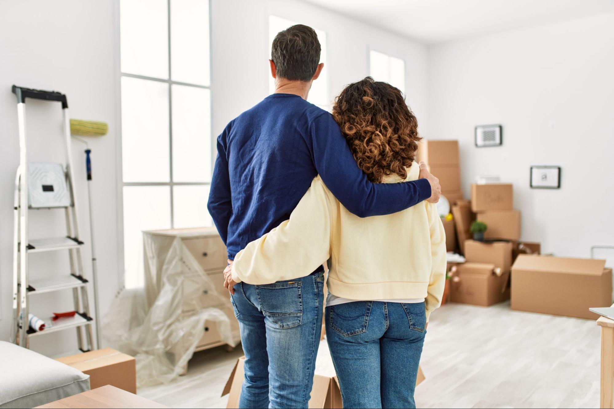 A couple with their arms around each other look at the home they’re moving into.
