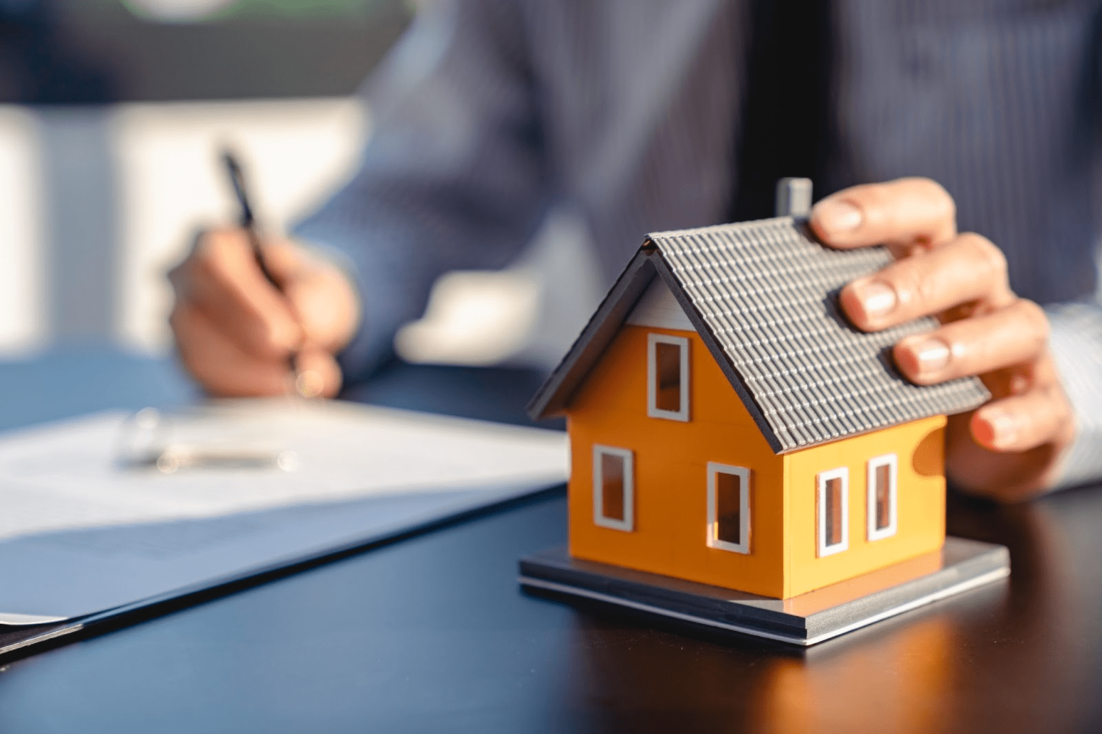 A person fills out a mortgage document and holds a small orange model home.