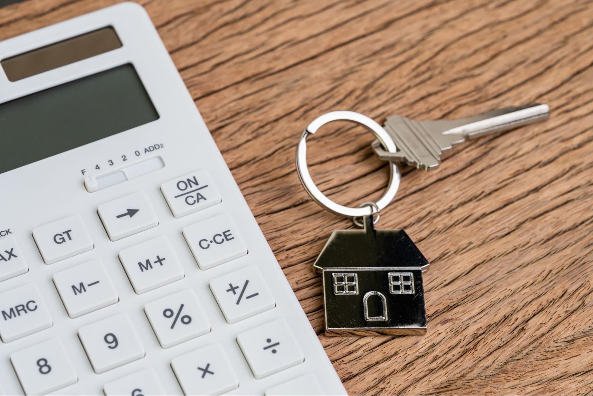 A house key sitting on a table beside a calculator. 