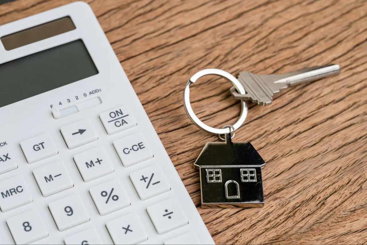 A house key sitting on a table beside a calculator.