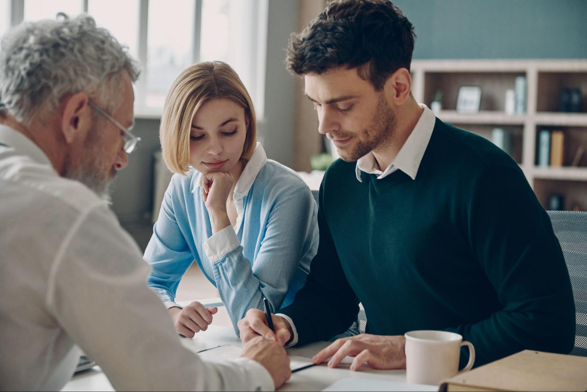 A young couple signing paperwork in their mortgage lender’s office