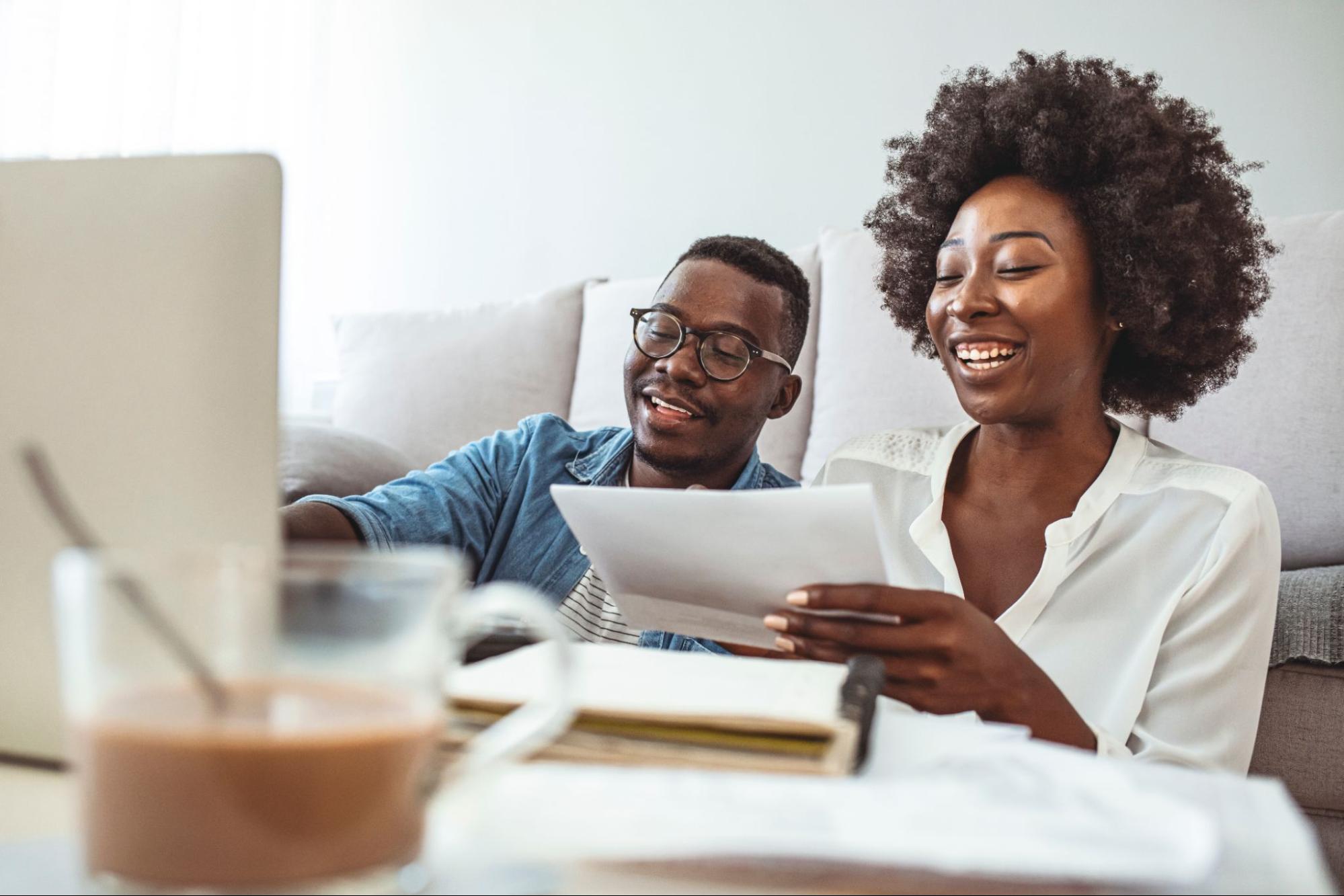 A young smiling couple sits in their living room reviewing mortgage documents.