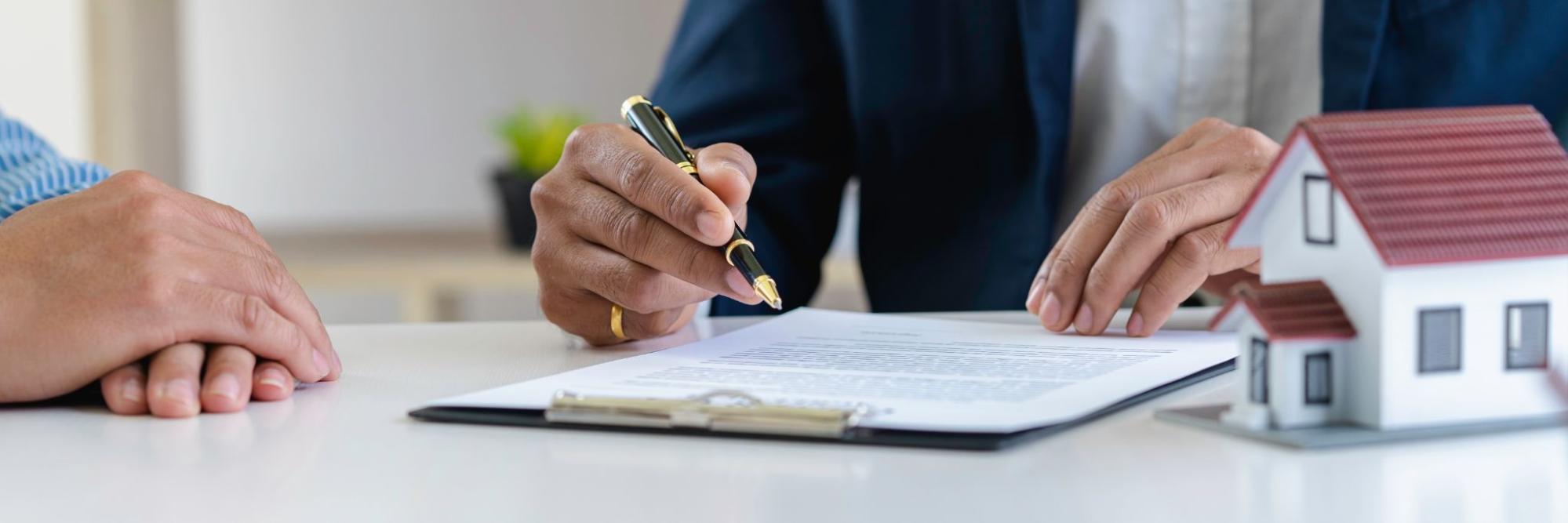 A person holding a pen reviews a contract sitting next to a model home. 