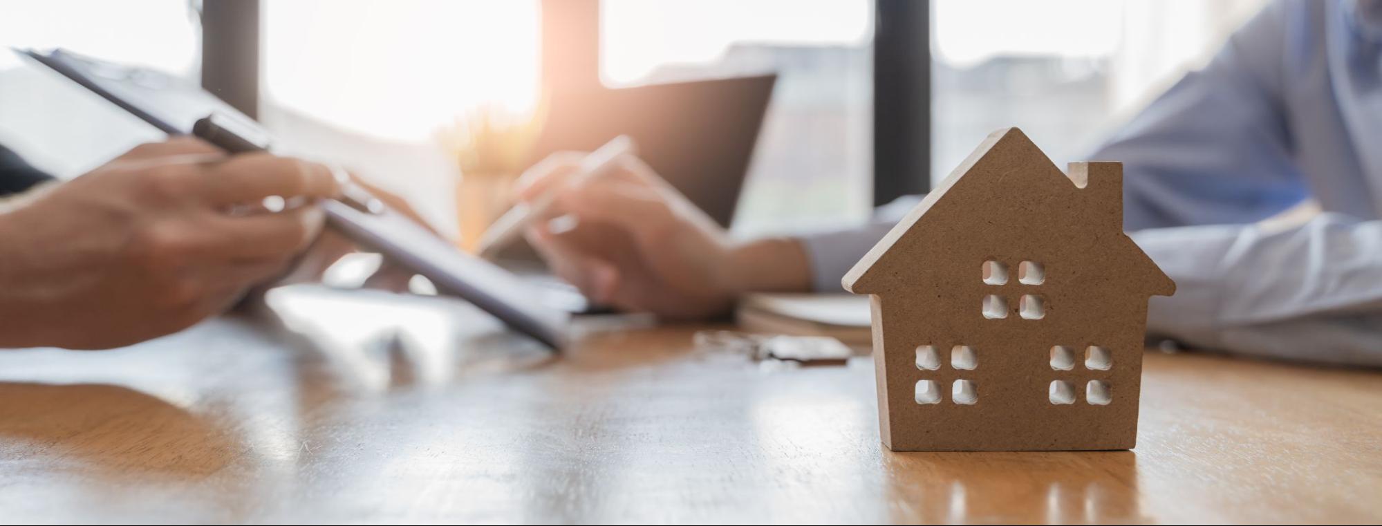 A lender and borrower review a contract behind a small model home.