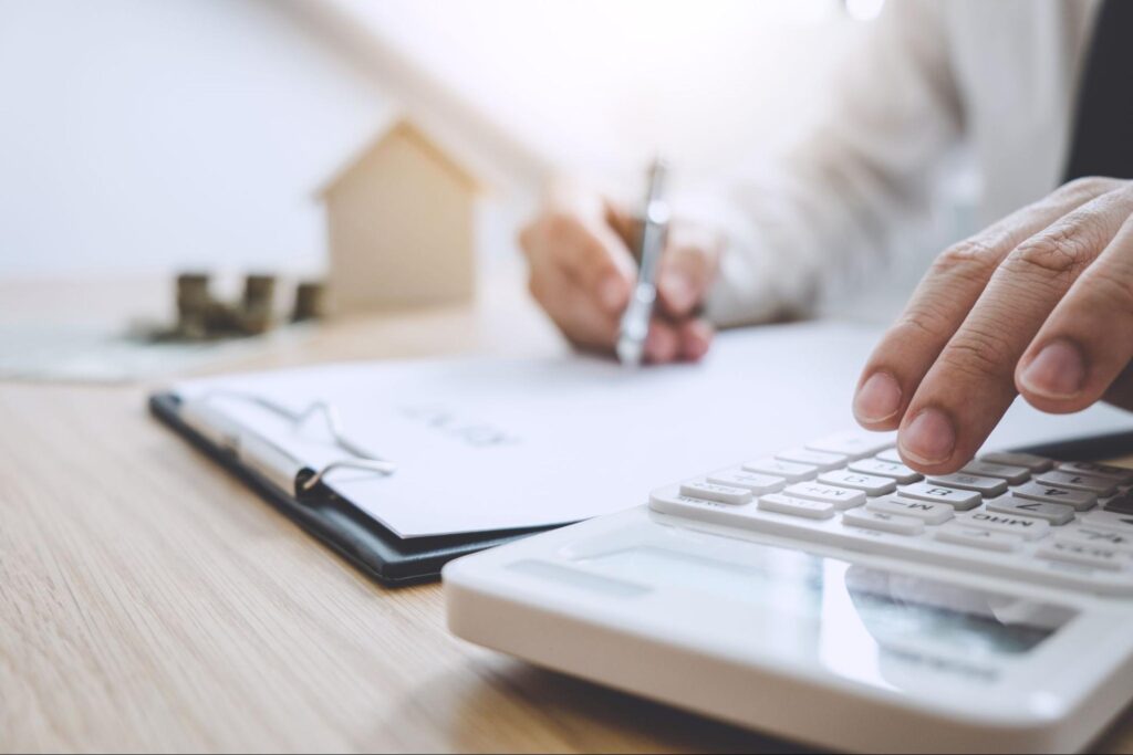 A person typing on a calculator with one hand and writing on a document with another.