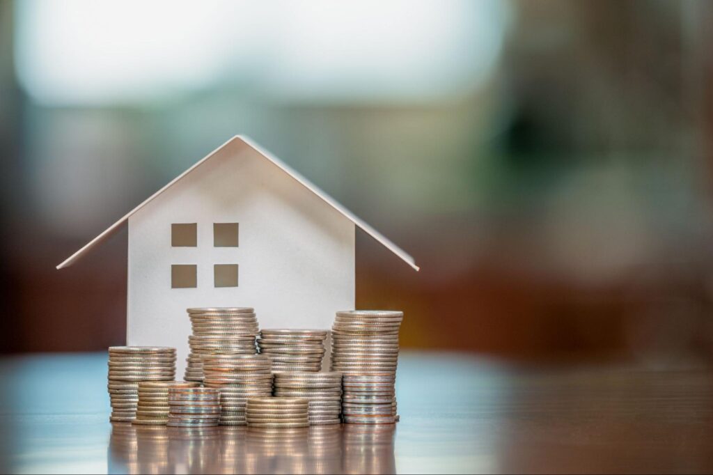 A white model home surrounded by stacks of coins.
