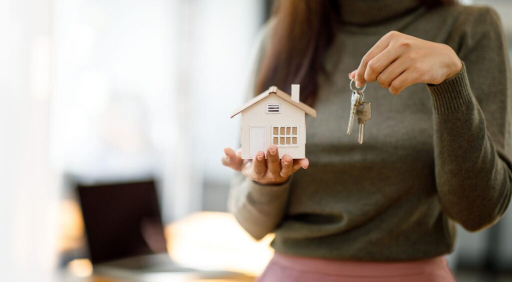 A woman holding up a model home in one hand and keys in the other.