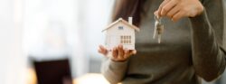A woman holding up a model home in one hand and keys in the other.