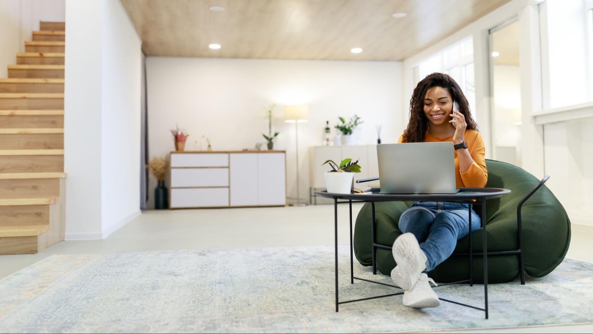 A woman on her phone working on her laptop in the living room of her mid-term rental.