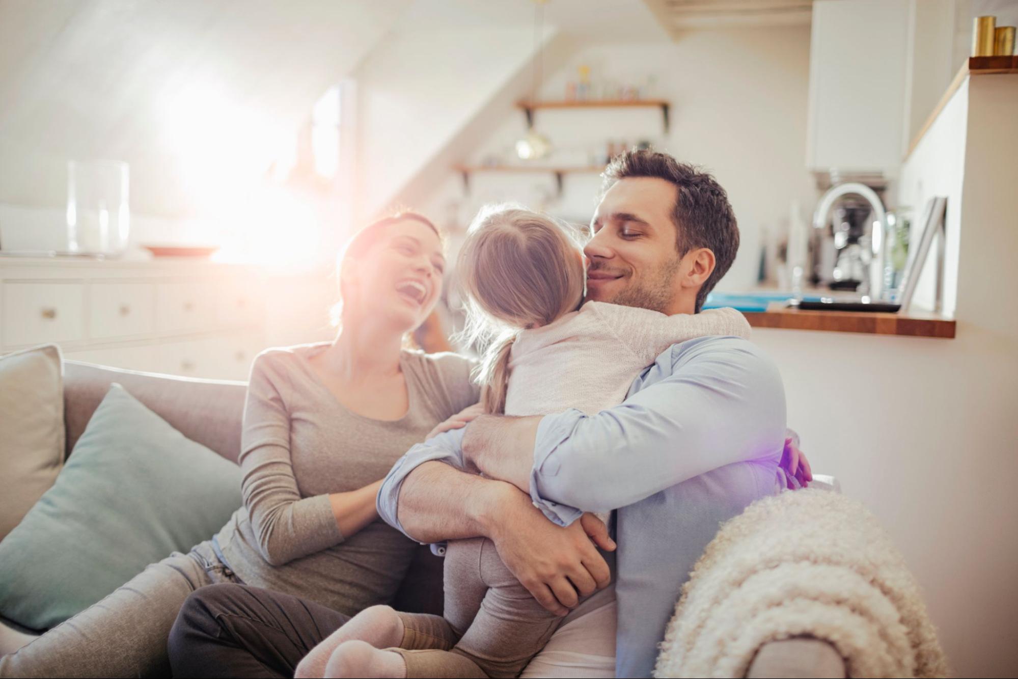 Smiling couple on the couch holding their young daughter. 