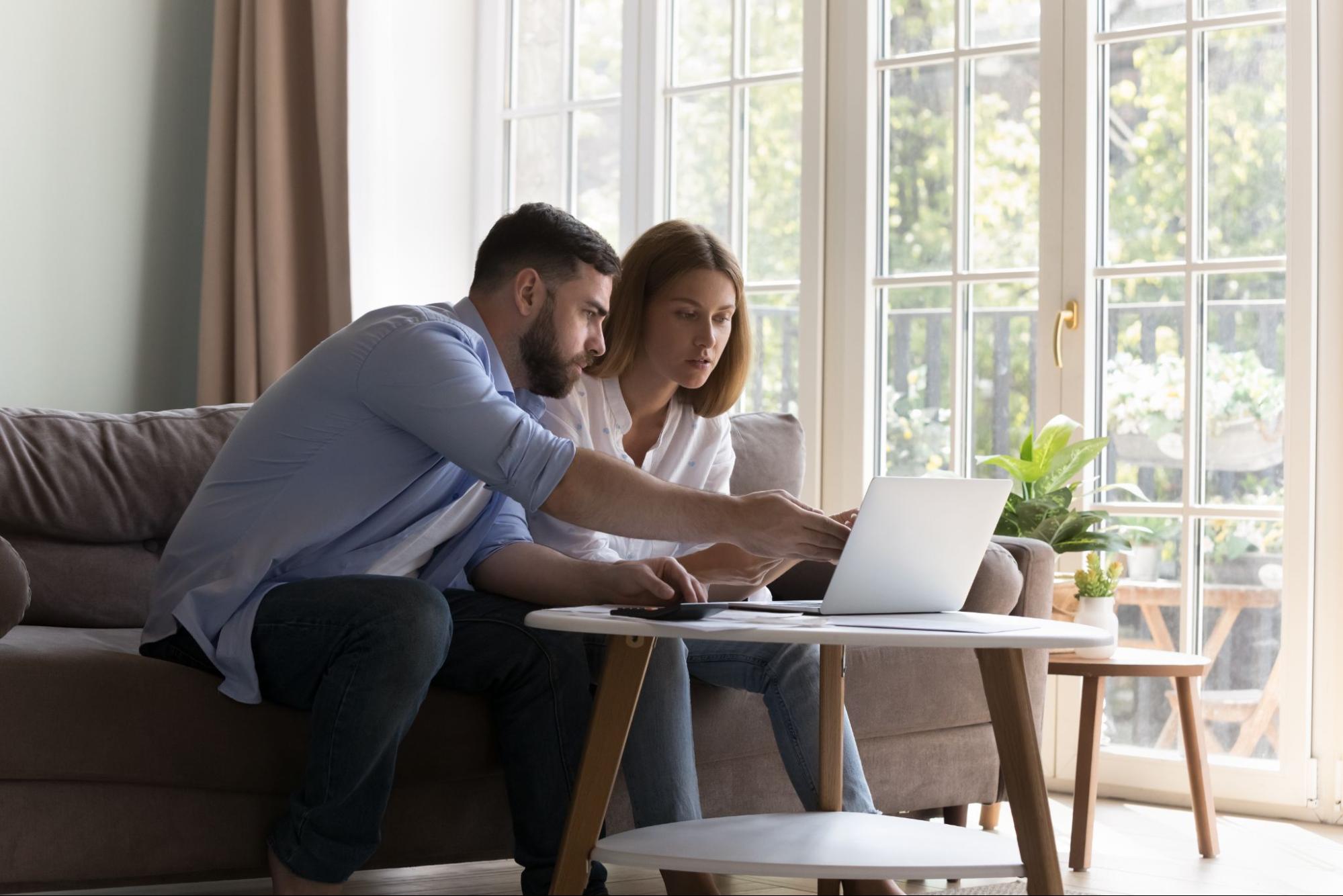 A couple sitting in their living room and reviewing mortgage documents on their laptop.