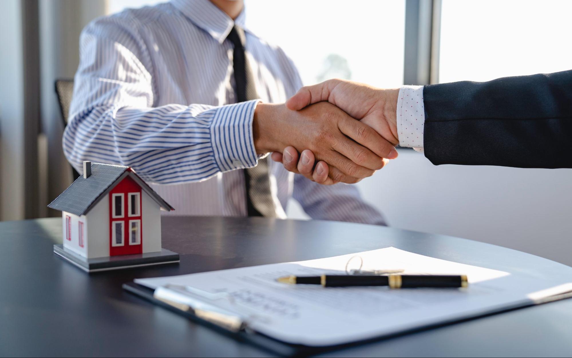 Two people shaking hands over a mortgage contract. 
