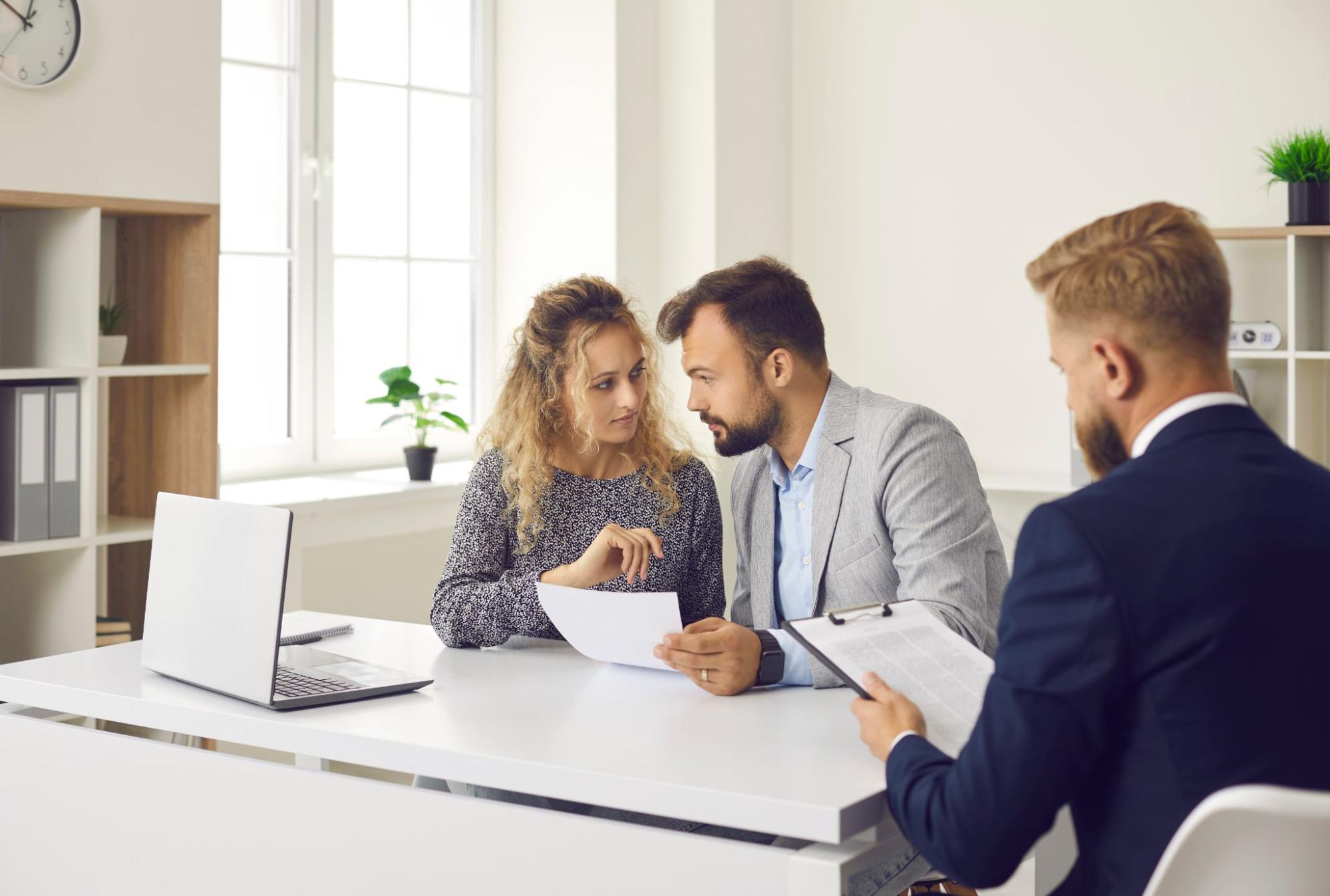 A couple sitting in their lender’s office reviews a mortgage contract. 