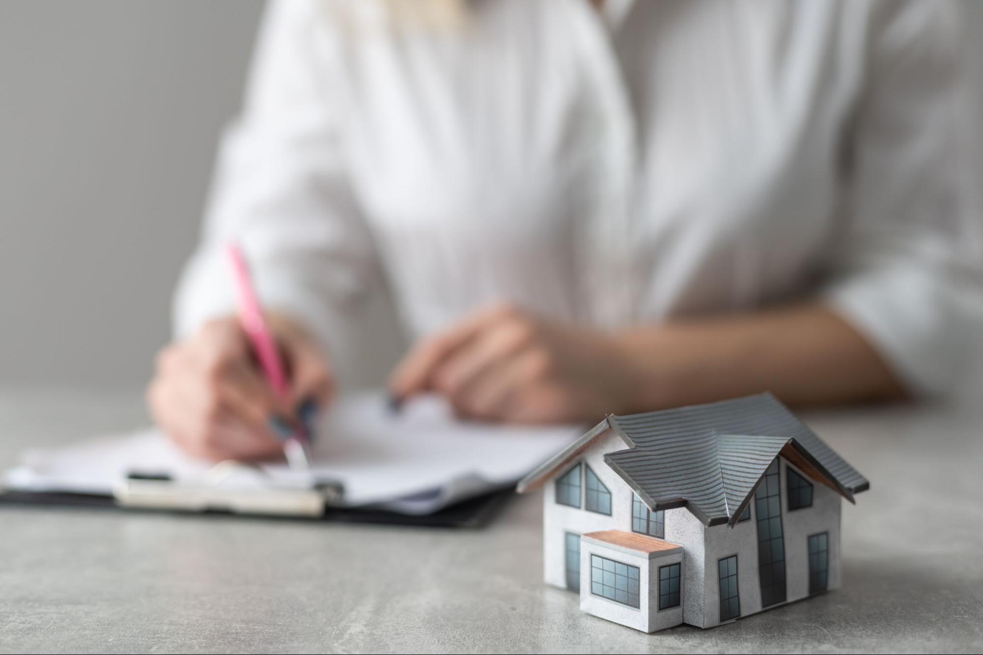 A woman writes out a contract with a model home sitting on the desk. 