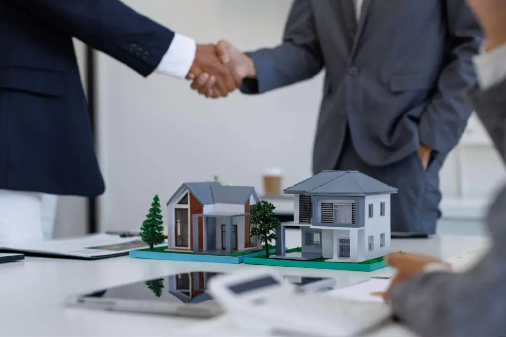 business partners shaking hands behind two model investment properties.