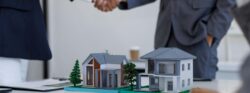 business partners shaking hands behind two model investment properties.