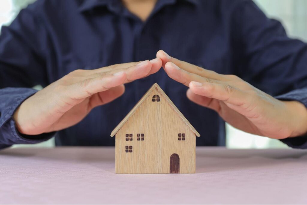 A person holding their hands over the roof of a model home.