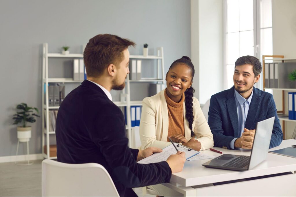 Smiling couple speaking with their realtor in his office.