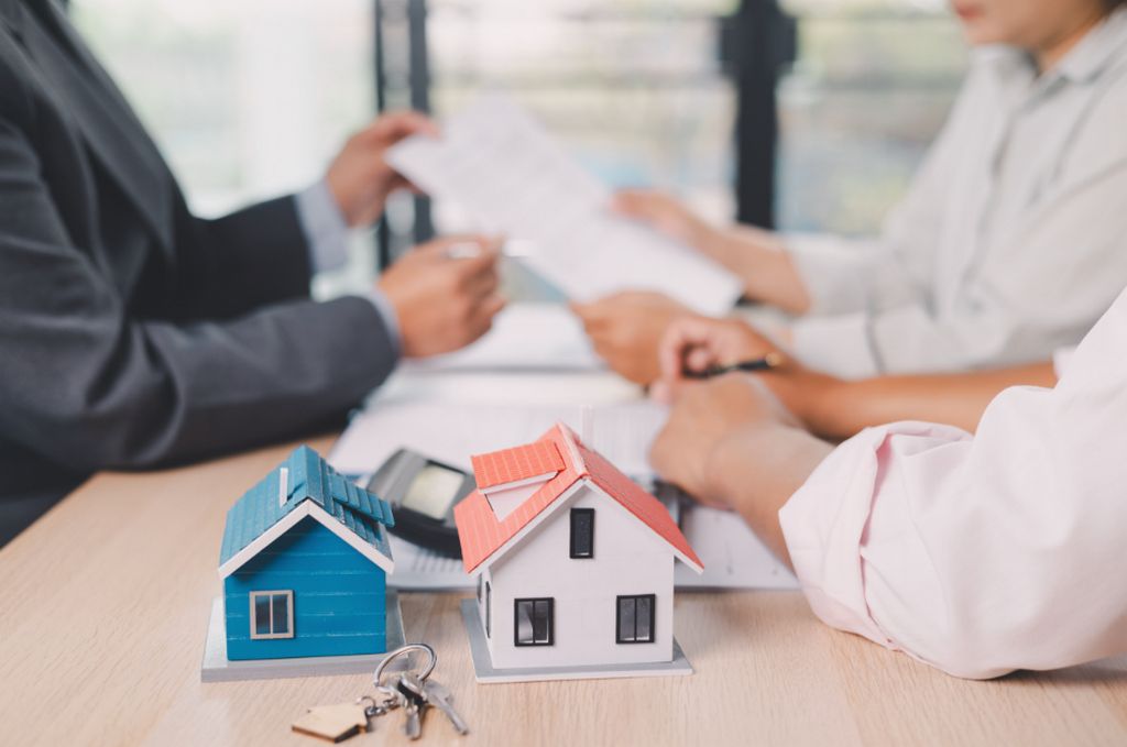 Two miniature houses and a set of keys on a table during a real estate meeting.