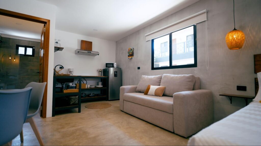 Modern vacation rental studio with a sofa, kitchenette, dining area, and large window.